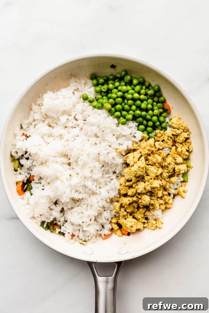 Savory Vegan Tofu Fried Rice 5 A medley of rice, scrambled tofu, and green peas being tossed with savory sauces in a pristine white pan.