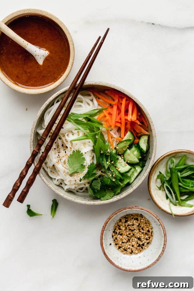 Spring Roll Power Bowls with Zesty Almond Butter Sauce 2 A spring roll noodle bowl with almond butter sauce on the side, garnished with sesame seeds and fresh herbs.