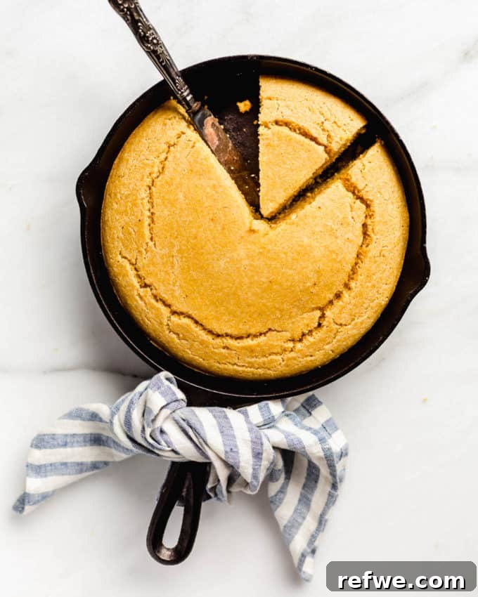 Plant-Based Cornbread 2 Golden vegan cornbread baked to perfection in a cast iron skillet, with a charming blue striped napkin wrapped around the handle, highlighting its rustic appeal.