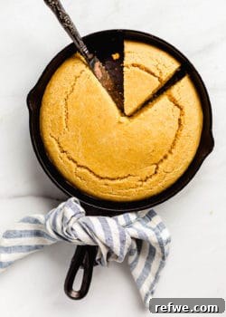 Golden vegan cornbread baked to perfection in a cast iron skillet, with a charming blue striped napkin wrapped around the handle, highlighting its rustic appeal.