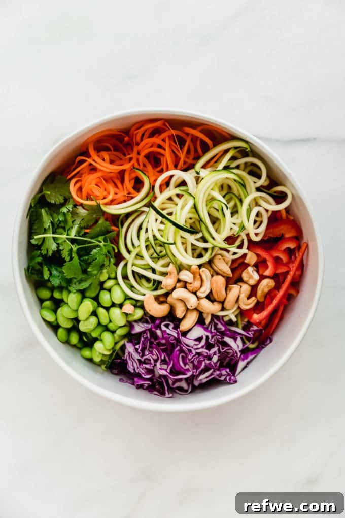 Vibrant Raw Pad Thai Noodles 4 A large white bowl filled with freshly spiralized zucchini and carrots, thinly sliced red bell pepper, finely shredded purple cabbage, bright green edamame, and fresh cilantro, all ready to be dressed.