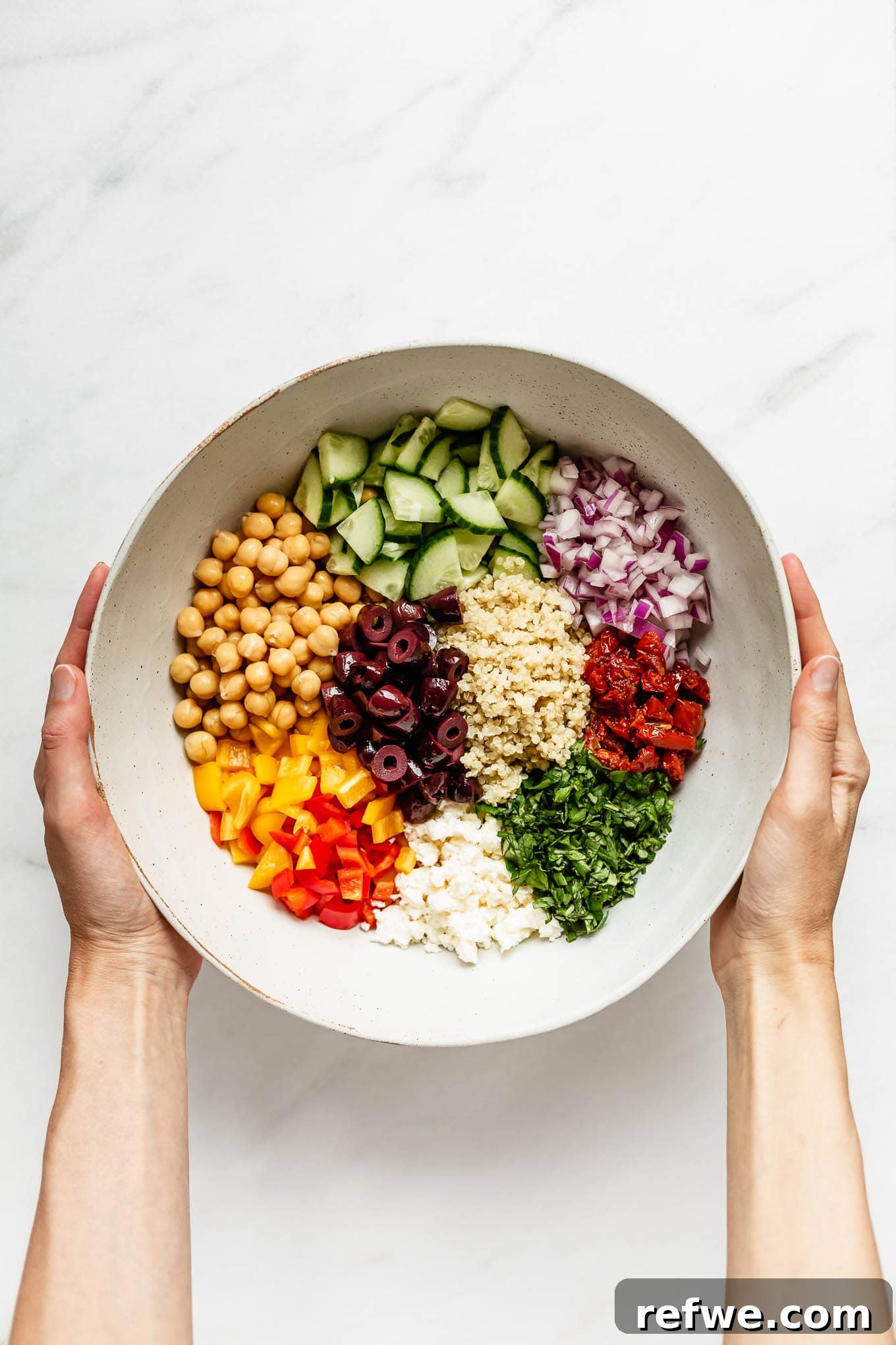 Vibrant Mediterranean Quinoa Bowl 4 Two hands holding a bowl of freshly prepared Mediterranean quinoa salad, highlighting the vibrant colors and textures.