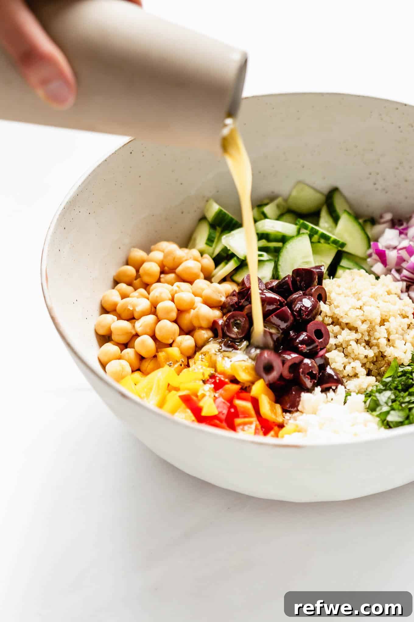 Vibrant Mediterranean Quinoa Bowl 5 A hand pouring the lemon oregano dressing into a bowl of vibrant quinoa salad ingredients.