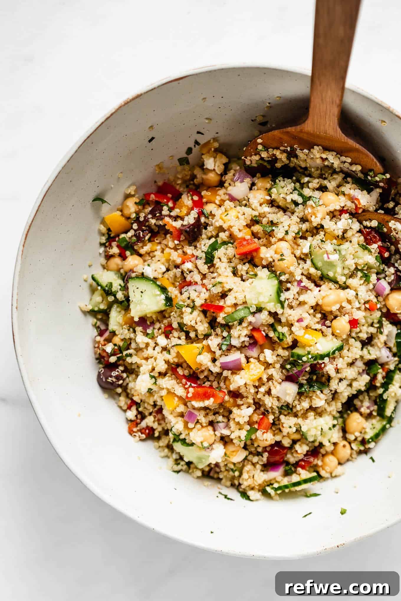 Vibrant Mediterranean Quinoa Bowl 6 A large bowl of Mediterranean quinoa salad with a wooden spoon, ready to be served.