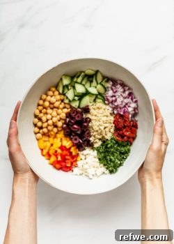 A mixing bowl filled with ingredients for a quinoa salad, held by two hands.