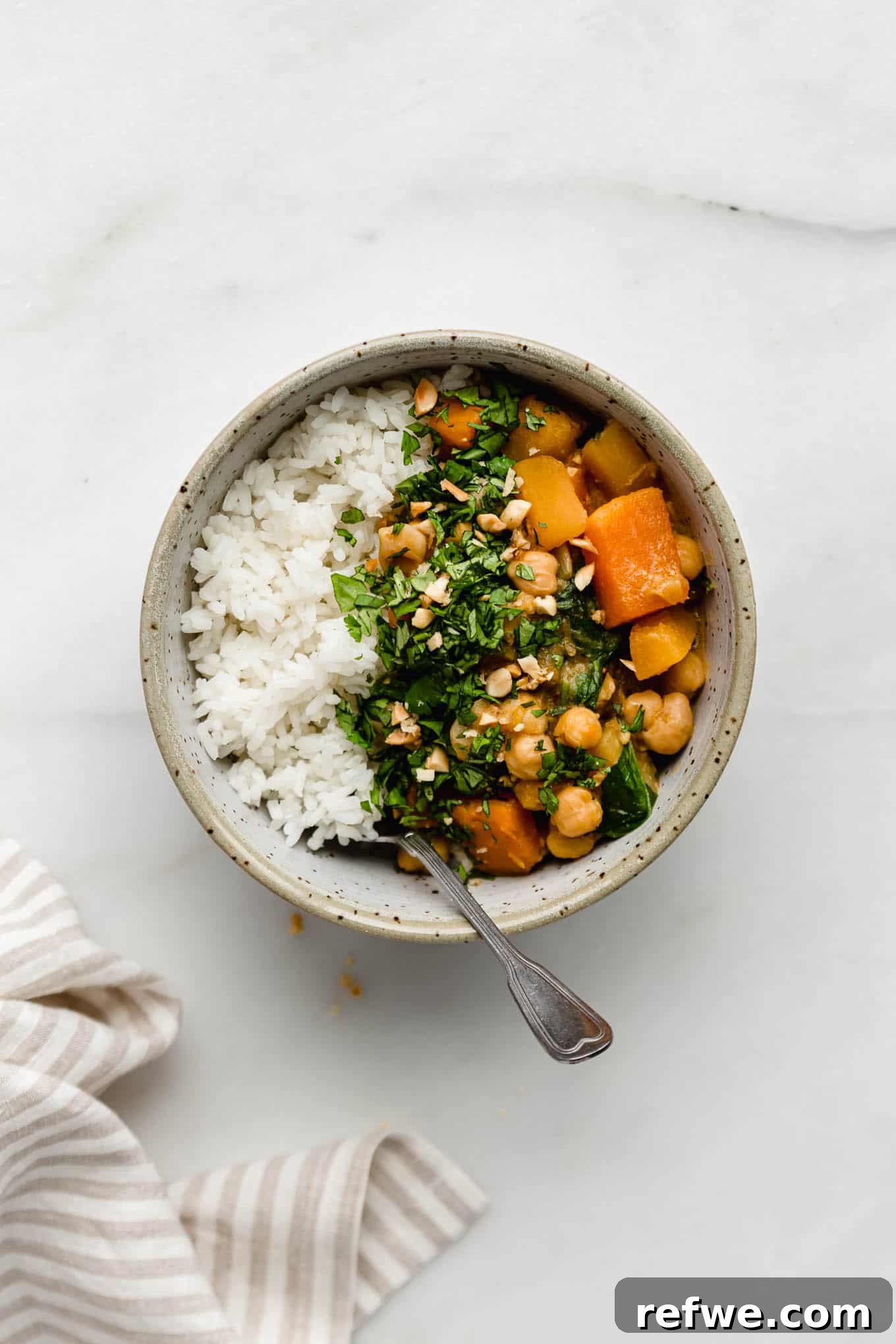 Hearty Slow Cooker Chickpea Pumpkin Curry 2 A vibrant bowl filled with white rice and a rich chickpea pumpkin curry, beautifully topped with fresh cilantro and crunchy crushed peanuts.