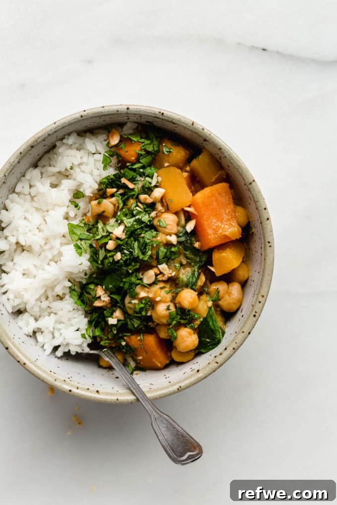 Hearty Slow Cooker Chickpea Pumpkin Curry 4 A serving of chickpea pumpkin curry with rice, garnished with fresh herbs, and a spoon in the bowl.