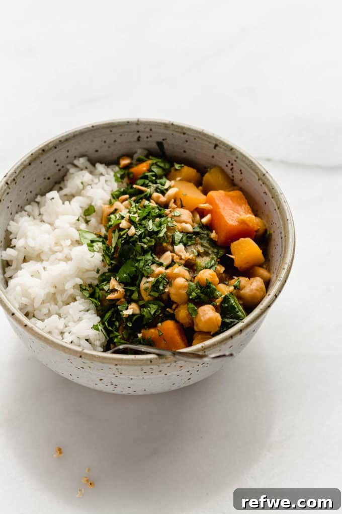 Hearty Slow Cooker Chickpea Pumpkin Curry 6 A speckled light blue bowl filled with rice, chickpeas, and a rich, creamy pumpkin curry, ready for dinner.