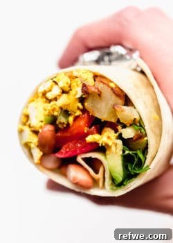 A hand holding a half of a vegan breakfast burrito