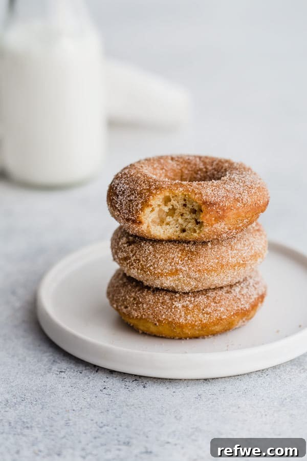 Freshly baked vegan pumpkin spice donuts being coated in cinnamon sugar.