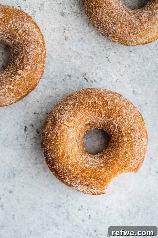 A stack of golden vegan pumpkin spice donuts with cinnamon sugar on a rustic surface.