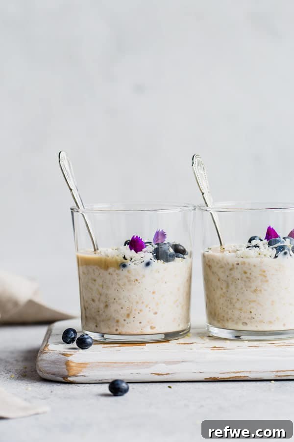 Effortless Overnight Steel Cut Oats 3 Two aesthetically arranged cups of overnight steel cut oats, adorned with various toppings, on a rustic white wooden serving board.