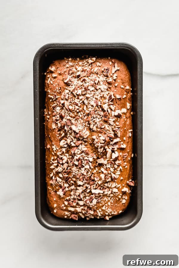 Wholesome Spiced Pumpkin Bread 7 A freshly baked pumpkin bread, golden brown and topped with pecans, still in its loaf pan on a cooling rack.