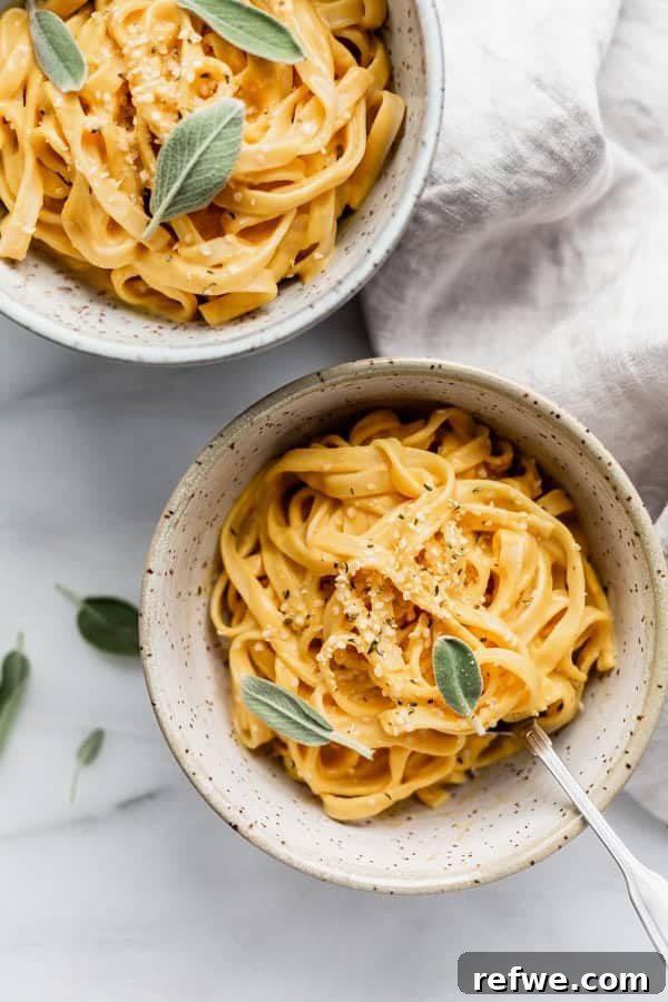 Creamy Plant-Based Pumpkin Alfredo Pasta 2 Two bowls of linguine pasta in a rich vegan pumpkin alfredo sauce, garnished with fresh sage leaves, ready to be served on a rustic wooden table.