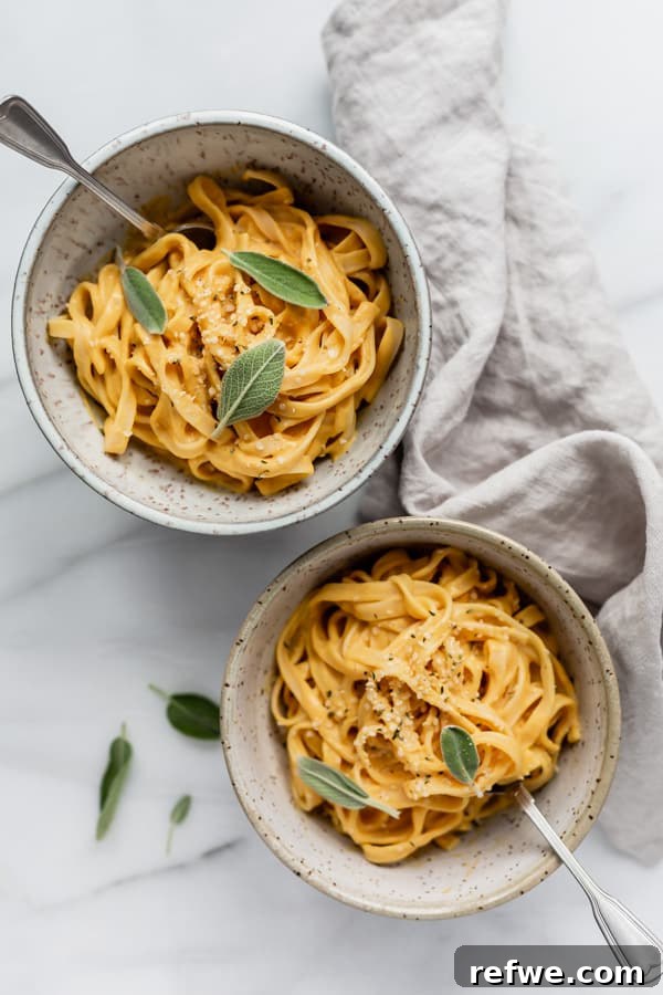 Creamy Plant-Based Pumpkin Alfredo Pasta 4 Two aesthetically arranged bowls of vegan pumpkin pasta, accompanied by a folded grey napkin, showcasing the vibrant orange sauce and green sage garnish.