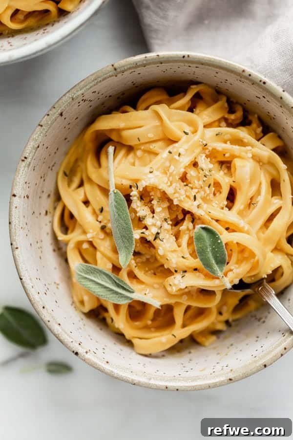 Creamy Plant-Based Pumpkin Alfredo Pasta 5 A single bowl of vegan pumpkin alfredo pasta, garnished with a fresh sage leaf, presented against a soft, blurred background, highlighting its inviting warmth.