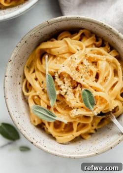A delectable bowl of vegan pumpkin Alfredo pasta, garnished with a fresh sage leaf, captured with a shallow depth of field, emphasizing its creamy texture and inviting presentation.