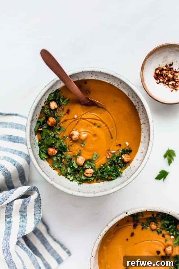 Golden Roasted Sweet Potato and Cinnamon Velouté 3 A vibrant bowl of roasted sweet potato cinnamon soup, accompanied by a striped napkin and a small dish of chili flakes for garnish.