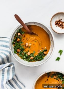 A bowl of roasted sweet potato cinnamon soup with a striped napkin on the side and a small dish of chilli flakes.