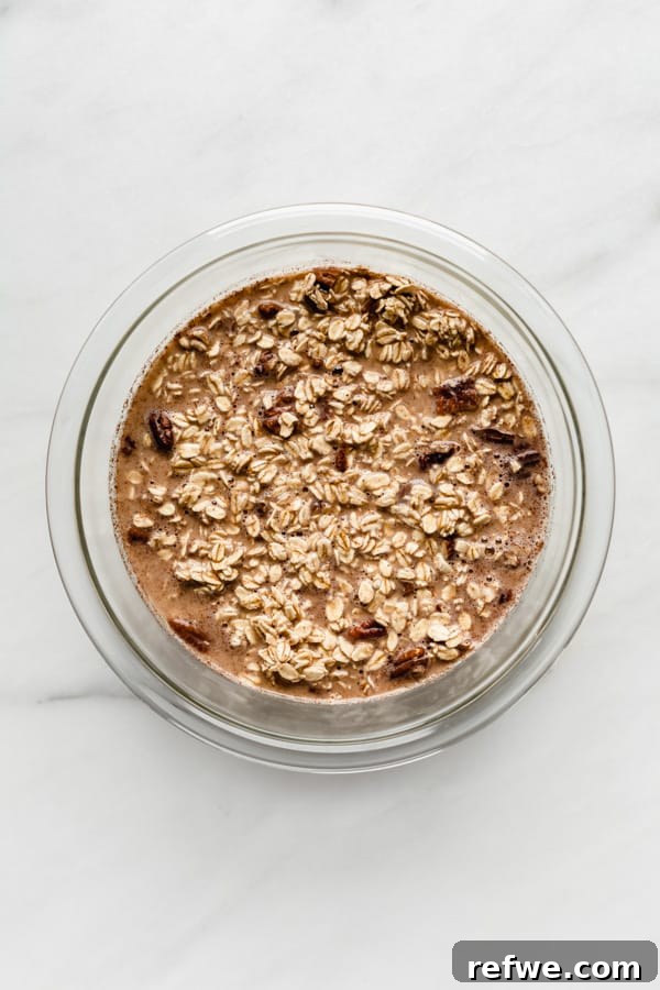A mixing bowl with rolled oats, almond milk, and chopped pecans, ready to be combined
