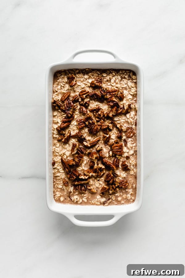 Unbaked pecan pie oatmeal in a white baking dish, topped with candied pecans before baking