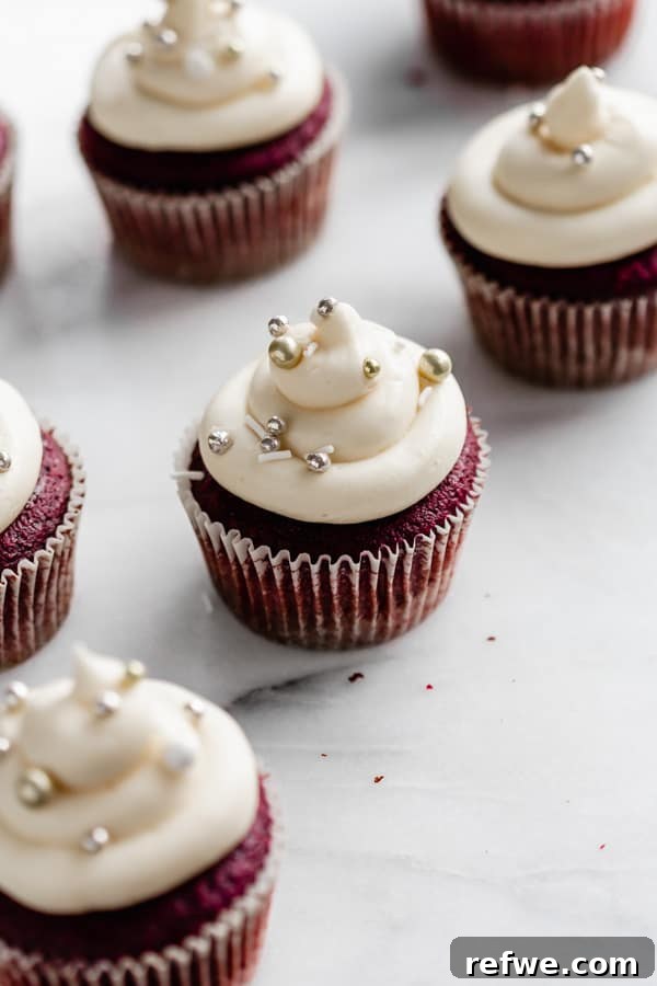 Luscious Vegan Red Velvet Cupcakes 4 vegan red velvet cupcakes on a marble board topped with white frosting and silver ball sprinkles