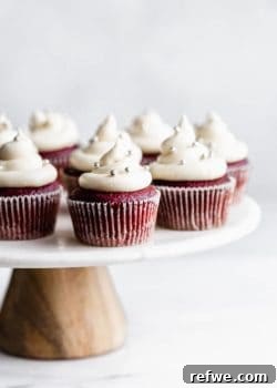 vegan red velvet cupcakes with cream cheese frosting and silver sprinkles on a marble and wood cakestand