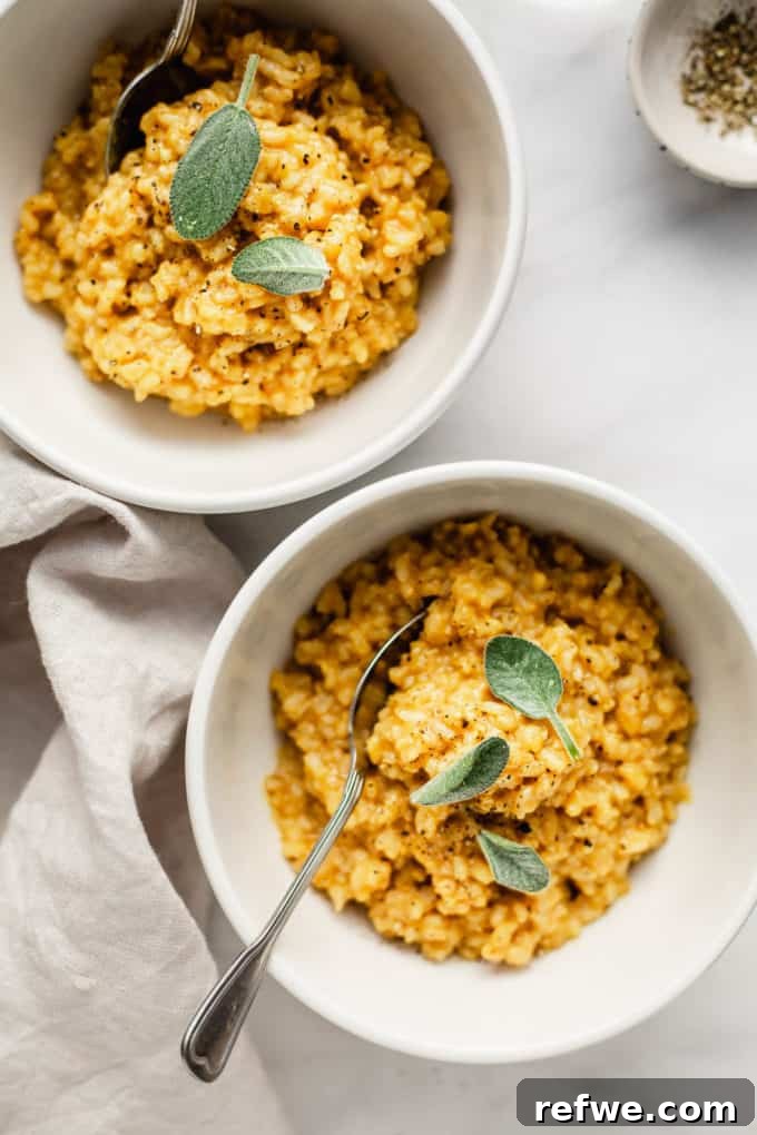 Two white bowls of creamy roasted butternut squash risotto, garnished with fresh sage and a small bowl of black pepper on the side.