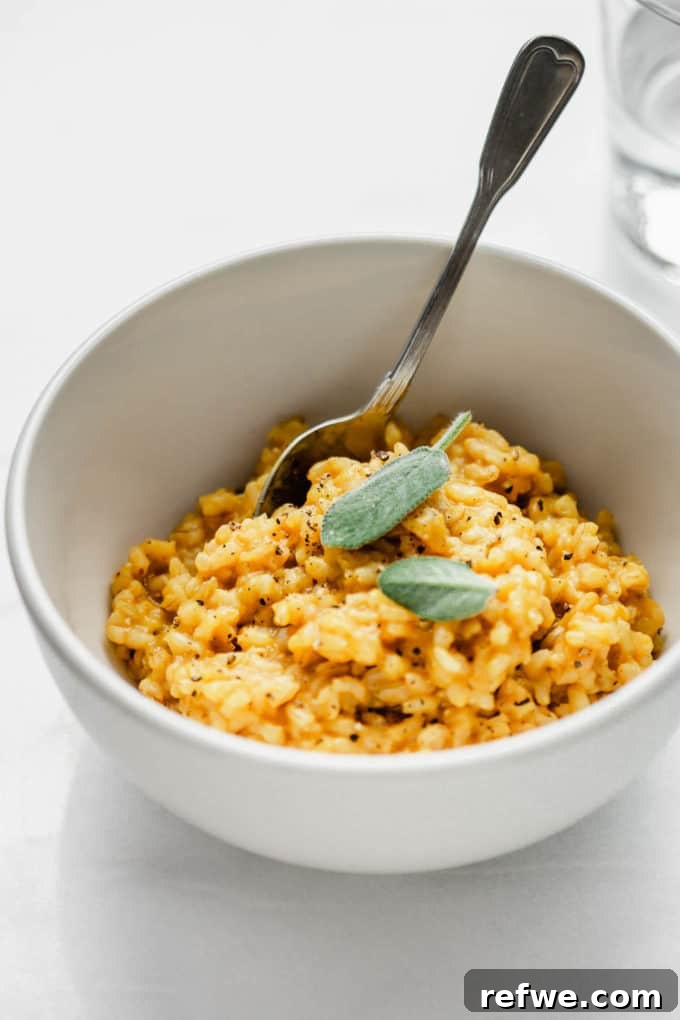 A beautifully presented white bowl with vibrant orange butternut squash risotto, garnished with fresh sage leaves on a rustic background.