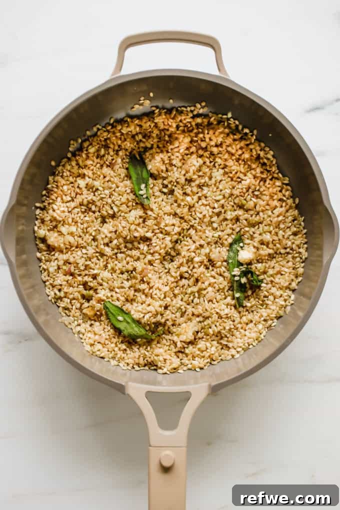 Arborio rice and fresh sage leaves being toasted in a pan with butter after aromatics.