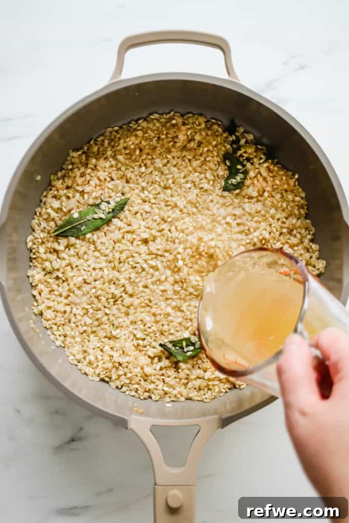 A hand carefully pouring warm vegetable broth into a pan of simmering risotto rice.