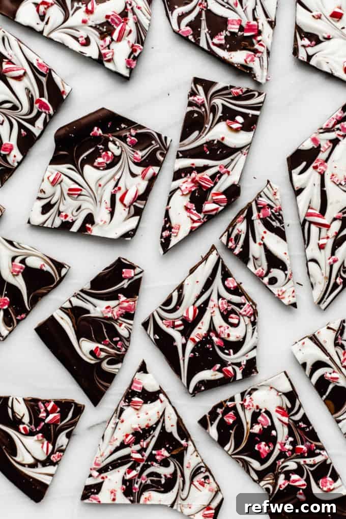 Wintermint Swirl Bark 2 Broken pieces of marbled peppermint bark on a festive marble tray, topped with crushed candy canes, ready to be enjoyed as a holiday dessert.