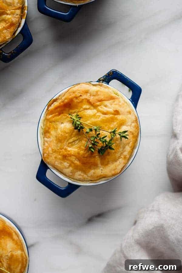 Effortless Garden Pot Pie 4 A close-up of a mini veggie pot pie with a golden puff pastry crust, garnished with a sprig of fresh thyme.