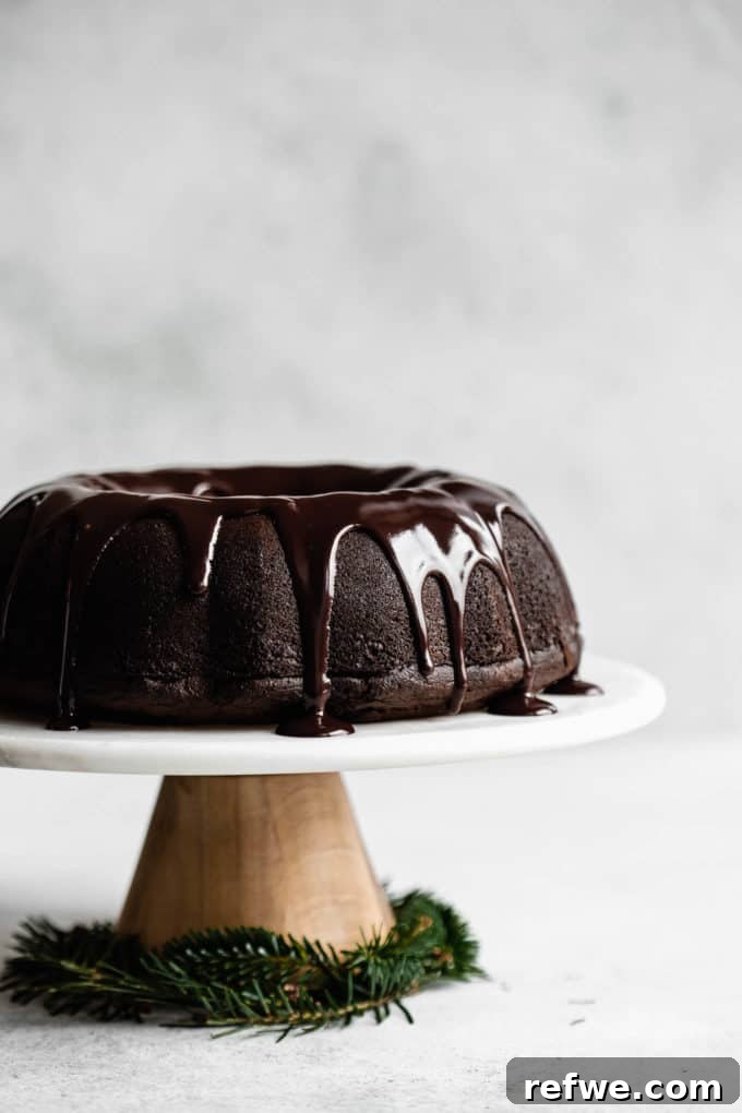 A gingerbread bundt cake topped with chocolate glaze on a marble and wooden cake stand, showing off its rich color and inviting topping.