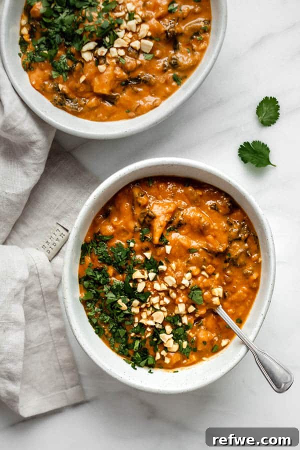 Cozy Vegan Peanut Pot 3 Two bowls of vibrant West African peanut stew, artfully arranged on a marble board with fresh cilantro leaves scattered nearby.
