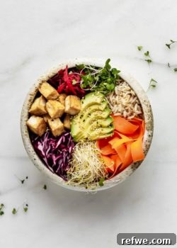 A close-up shot of a beautifully arranged Dragon Bowl with avocado, fresh vegetables, golden crispy tofu, and brown rice, topped with sauce.