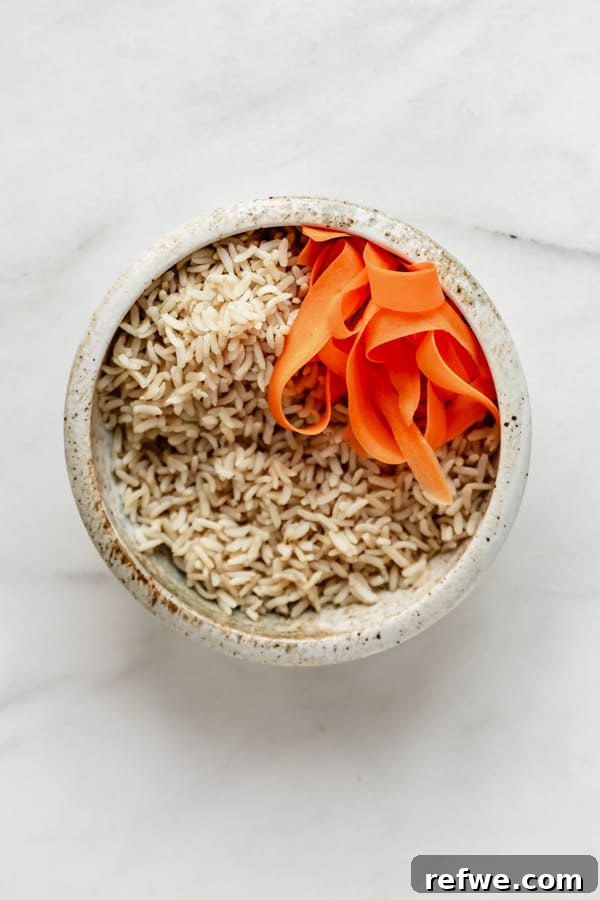Legendary Dragon Bowls 4 Brown rice in a ceramic bowl, topped with a colorful mound of shredded carrots, adding a pop of color and sweetness.