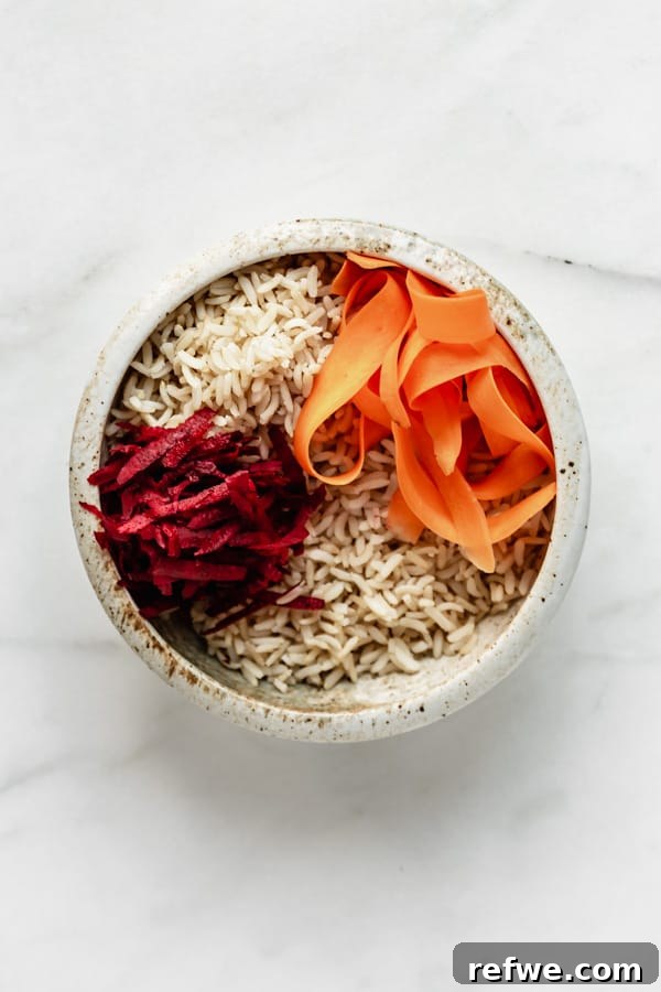 Legendary Dragon Bowls 5 A ceramic bowl featuring brown rice, vibrant shredded beets, and thinly sliced carrots, creating a beautiful color contrast.