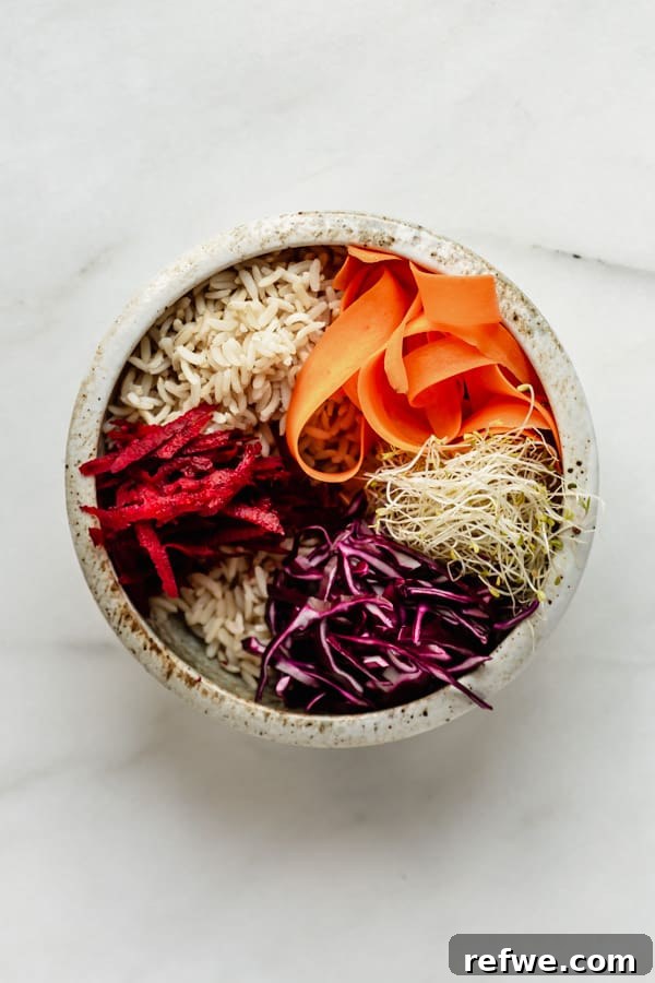 Legendary Dragon Bowls 7 A white ceramic bowl filled with brown rice and a colorful array of fresh vegetables, including cabbage, beets, and carrots.