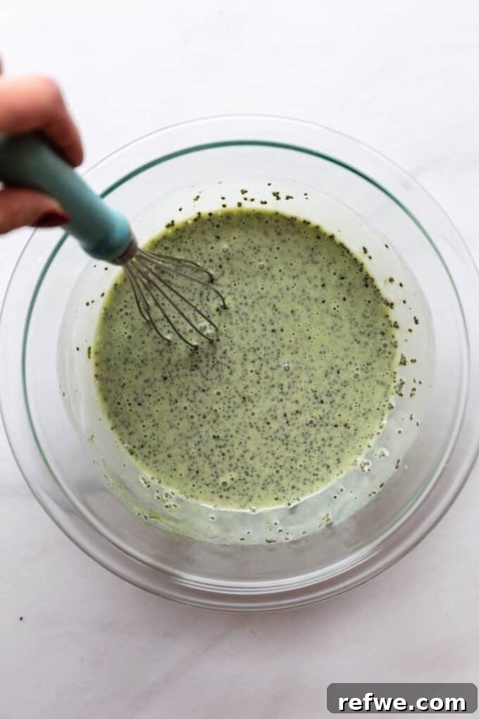 Vibrant Matcha Chia Pudding 5 A hand whisking the matcha chia pudding mixture in a glass mixing bowl, creating a smooth, vibrant green liquid.