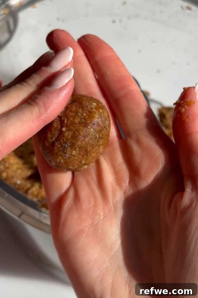 Two hands rolling a carrot cake energy ball from the prepared dough.