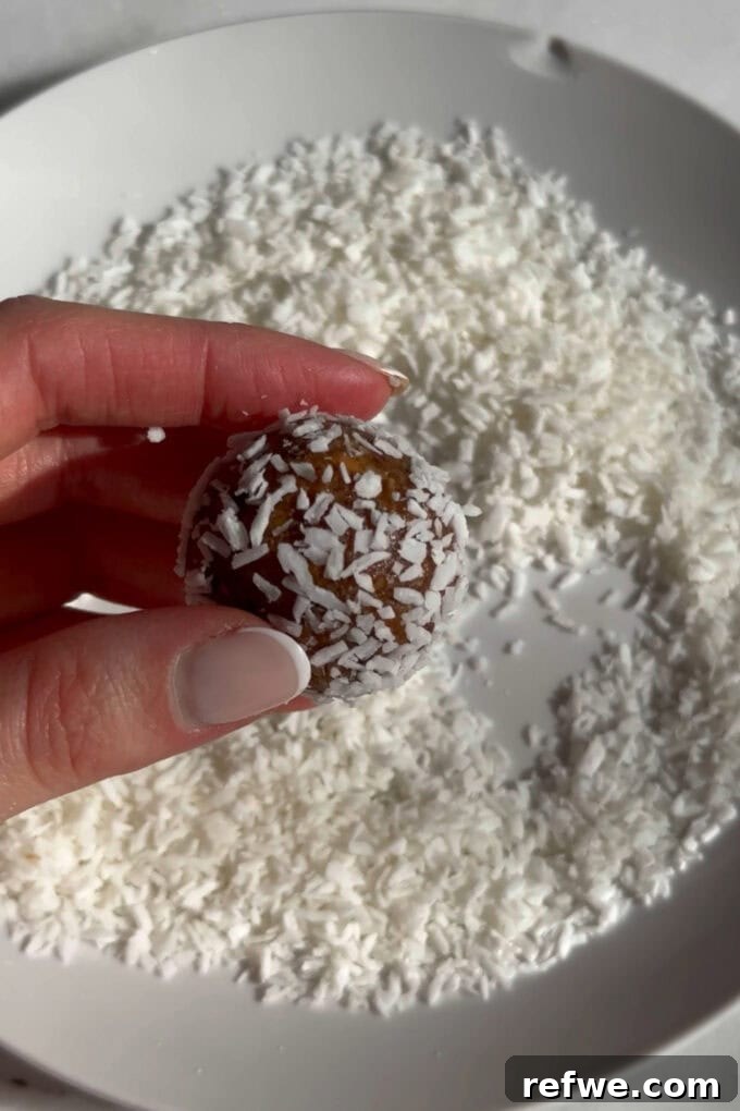 A carrot cake energy ball being rolled in shredded coconut for coating.
