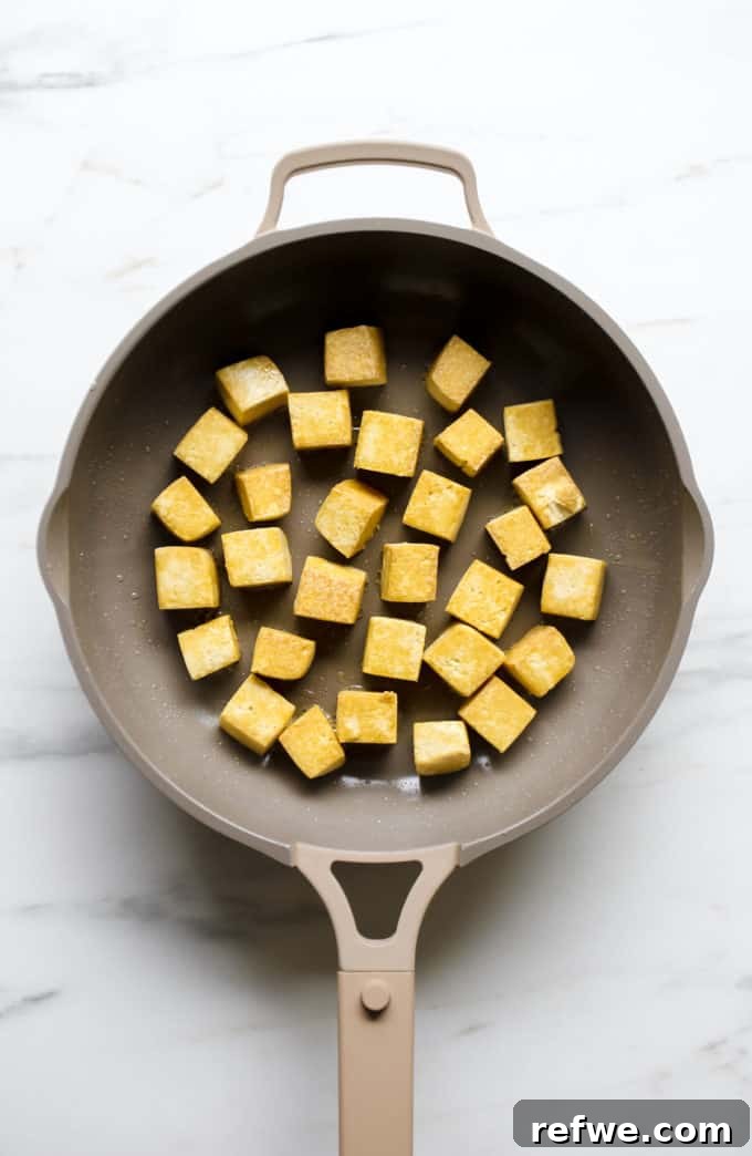 Creamy Thai Coconut Tofu Curry 5 Golden-brown tofu cubes sizzling in a frying pan, showcasing their crispy texture.