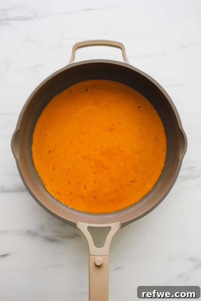 Creamy Thai Coconut Tofu Curry 6 A rich, red coconut curry sauce simmering gently in a saucepan, its vibrant color and smooth texture evident.