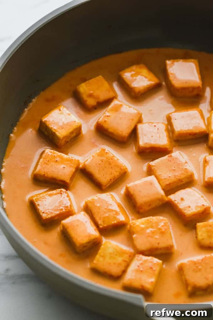 Creamy Thai Coconut Tofu Curry 7 Close-up view of crispy tofu cubes generously coated in a rich, red curry sauce within a frying pan.