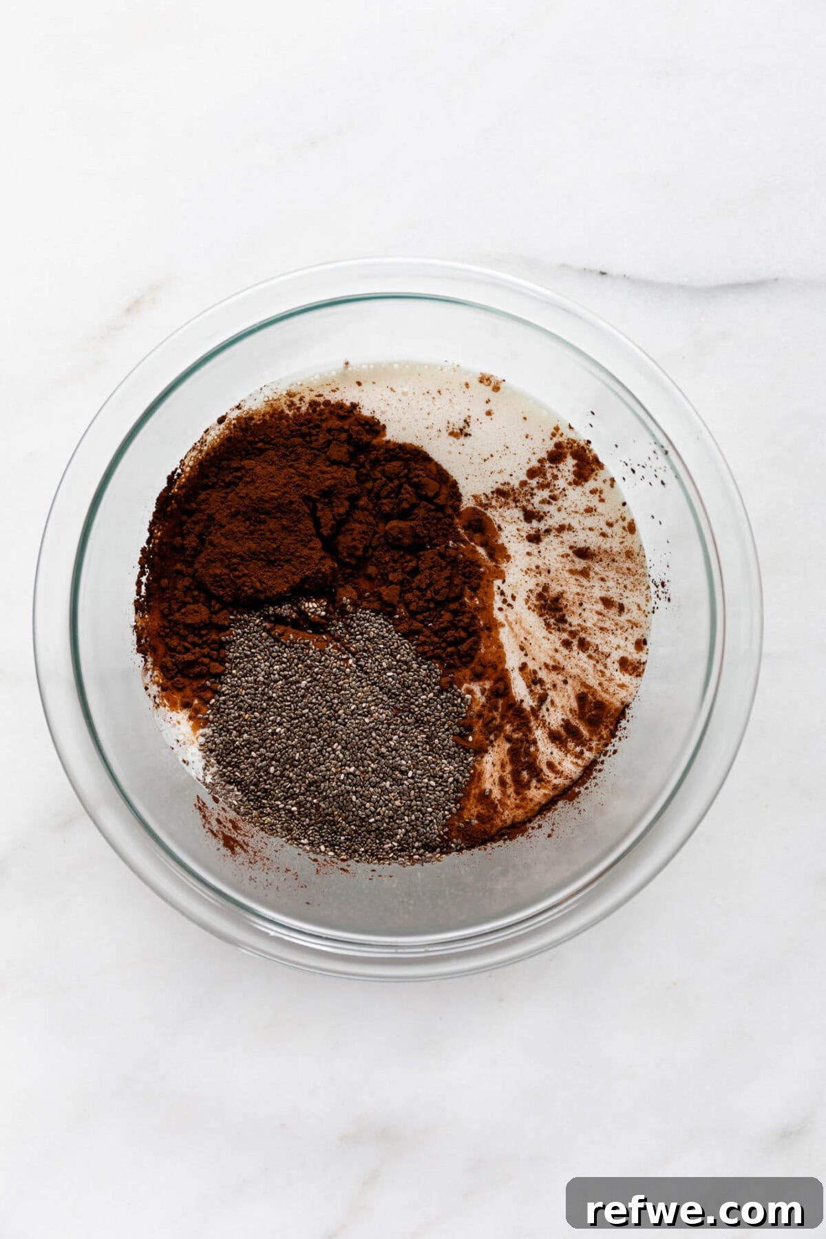 Silky Chocolate Chia Pudding 6 The smooth blended cottage cheese mixture is poured into a mixing bowl, and cocoa powder along with chia seeds are added on top, ready to be combined.
