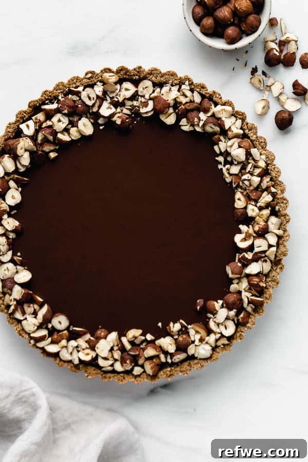 Decadent Vegan Chocolate Hazelnut Tart 4 A chocolate hazelnut tart topped with crushed hazelnuts and a slice removed