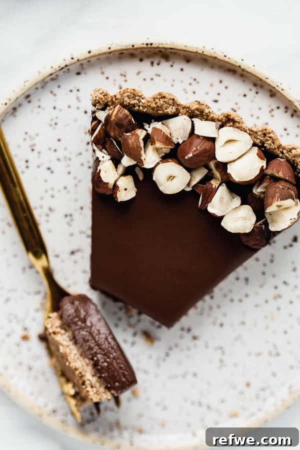 Decadent Vegan Chocolate Hazelnut Tart 6 A slice of vegan chocolate hazelnut tart on a plate, with whole hazelnuts