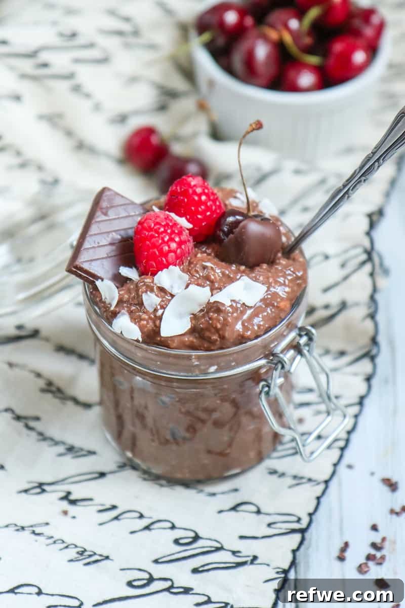 Decadent Brownie Batter Overnight Oats 3 Close-up of creamy brownie batter overnight oats topped with fresh raspberries and a spoon, ready to eat.