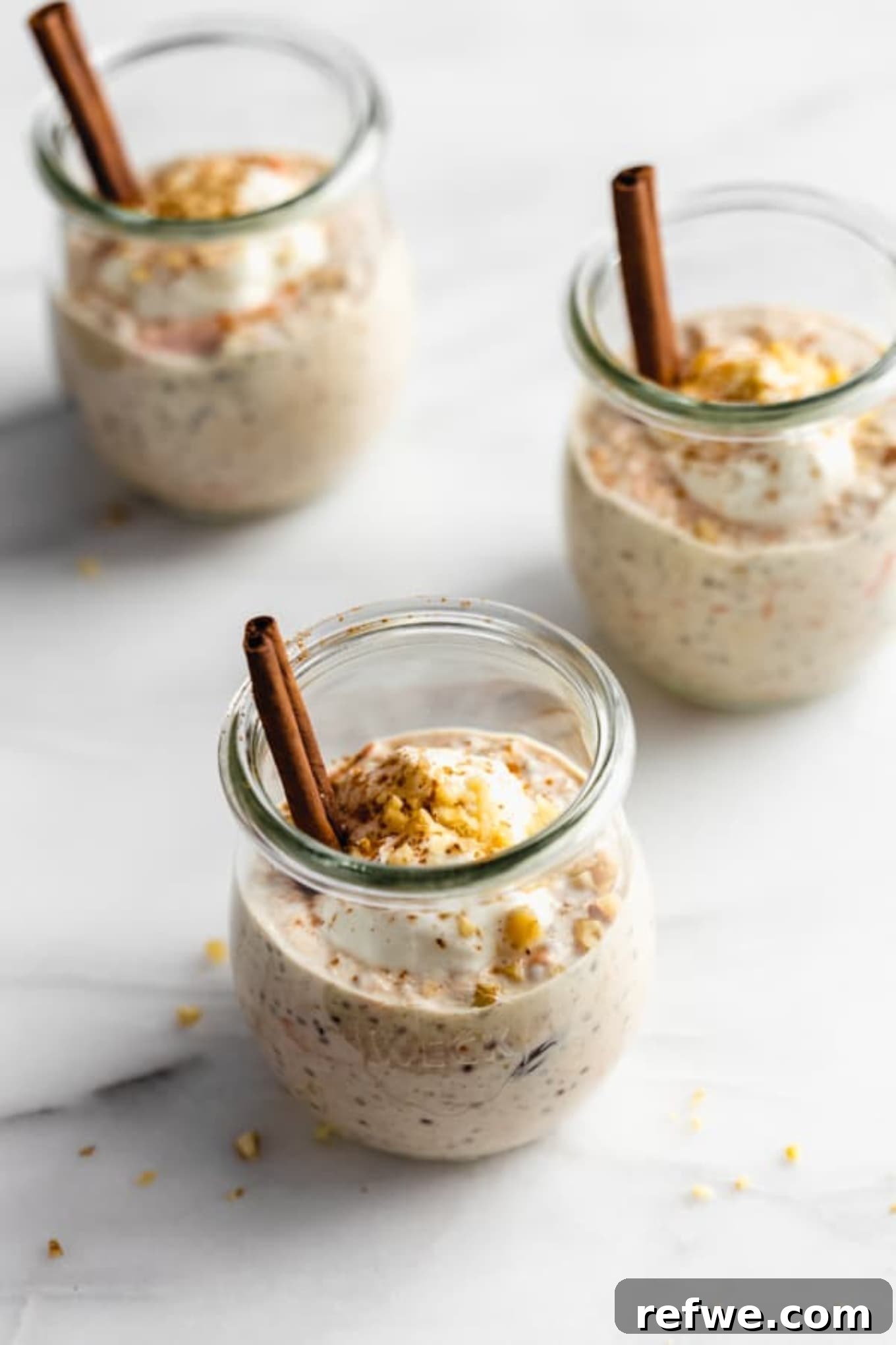 Three jars of carrot cake overnight oats, topped with yogurt, walnuts, and a sprinkle of cinnamon, ready for a healthy breakfast.